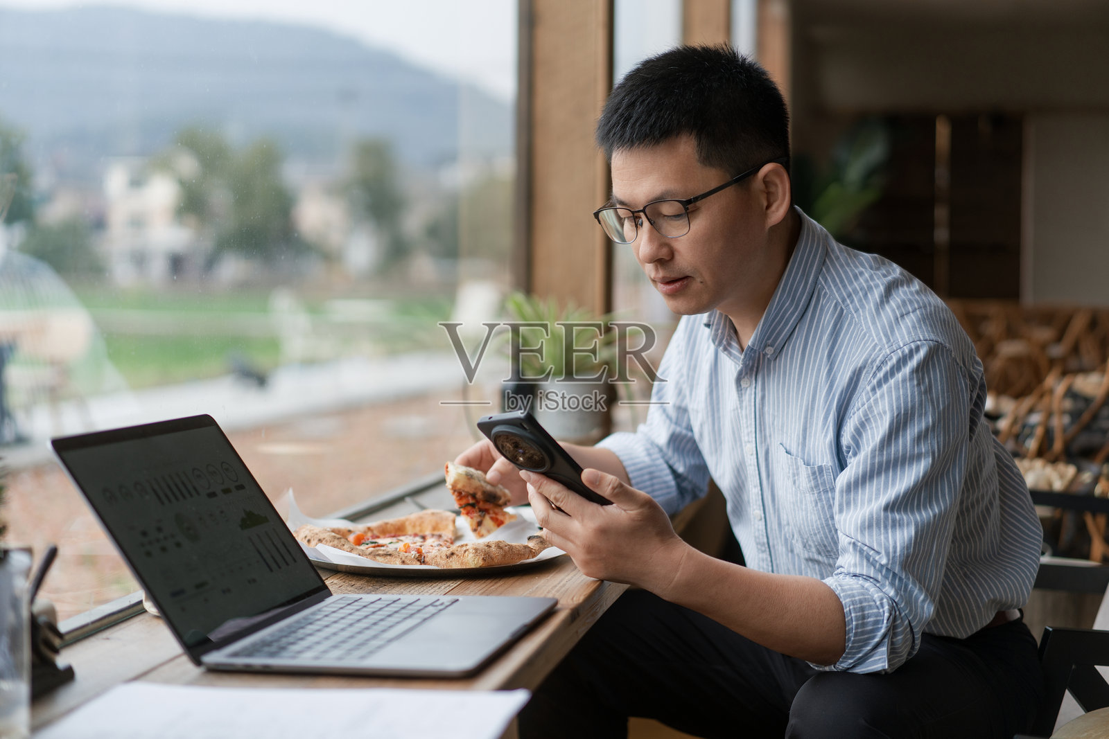 戴眼镜男子咖啡馆用手机看数据吃披萨照片摄影图片