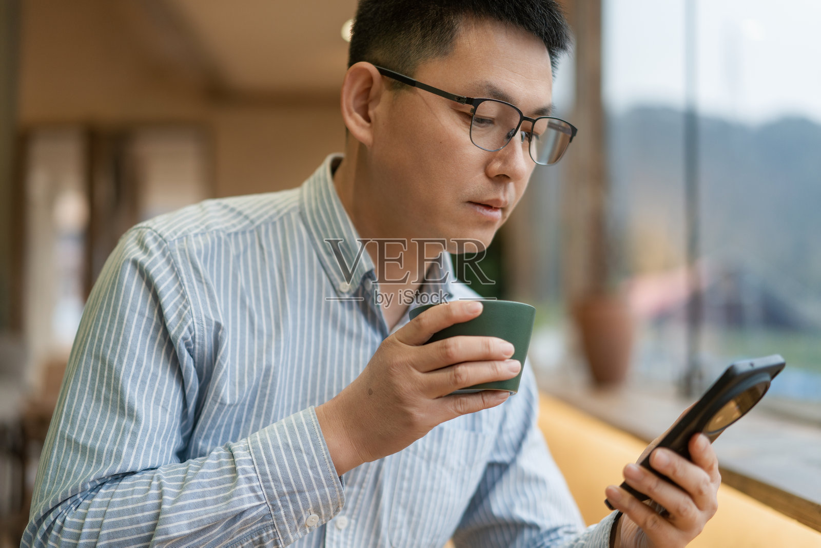 戴眼镜男子手持咖啡杯看手机照片摄影图片