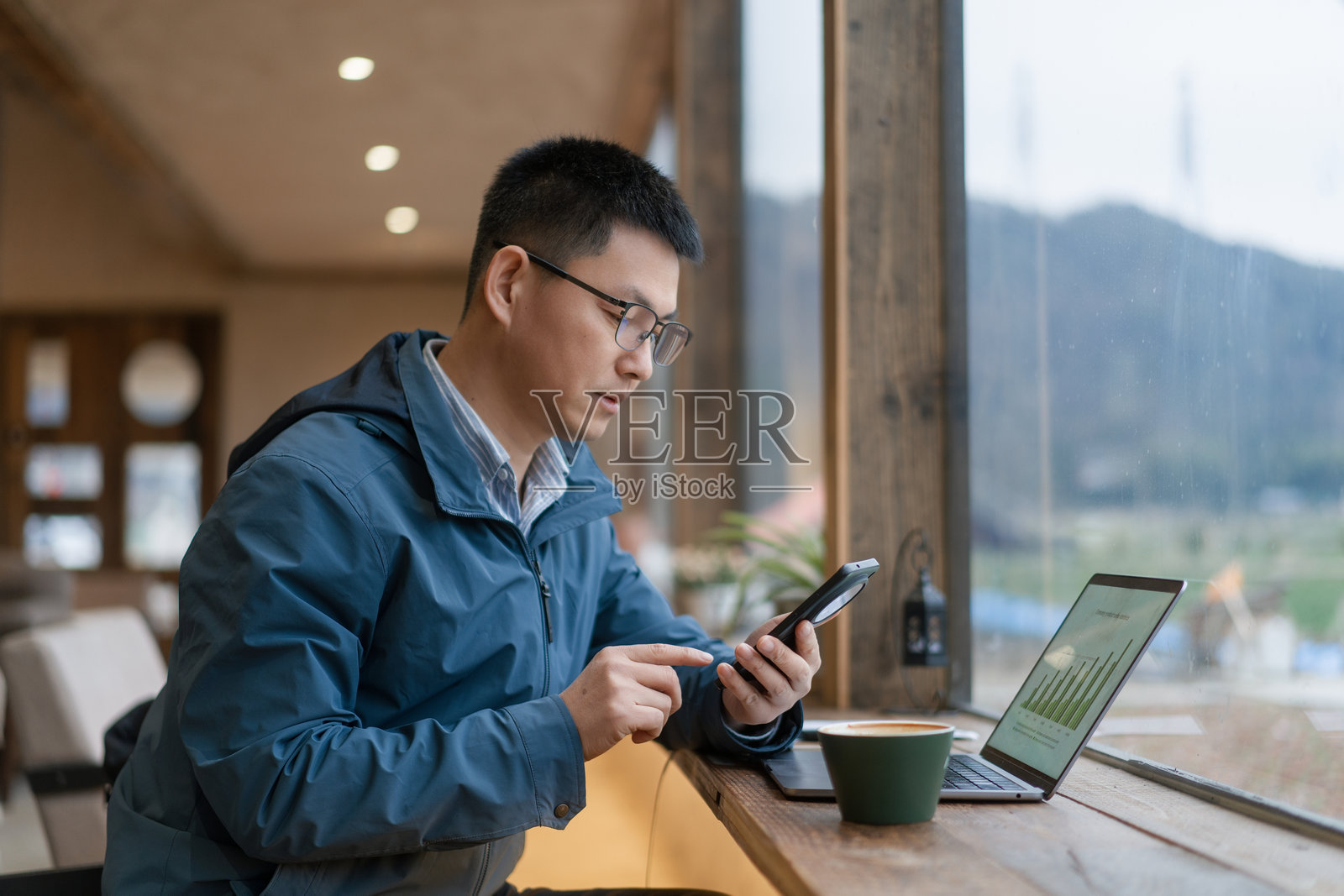 戴眼镜男子窗边用手机看数据查资料照片摄影图片