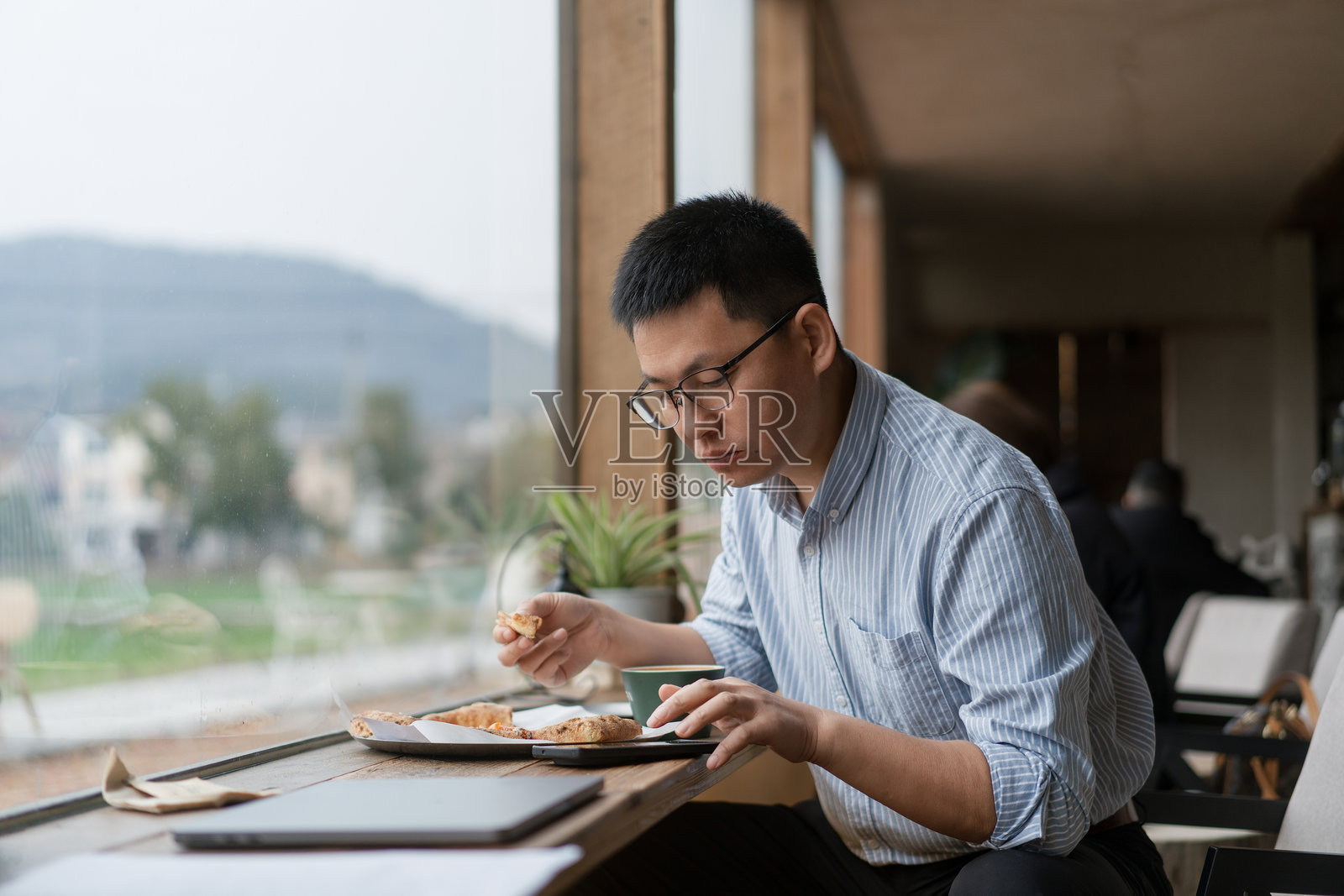 戴眼镜男子窗边用餐看平板电脑照片摄影图片