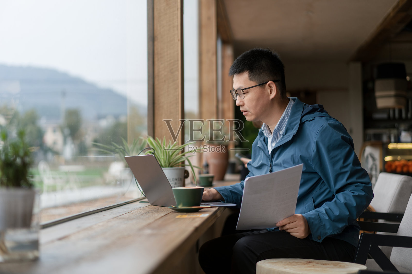 男子窗边用笔记本电脑查阅文件照片摄影图片