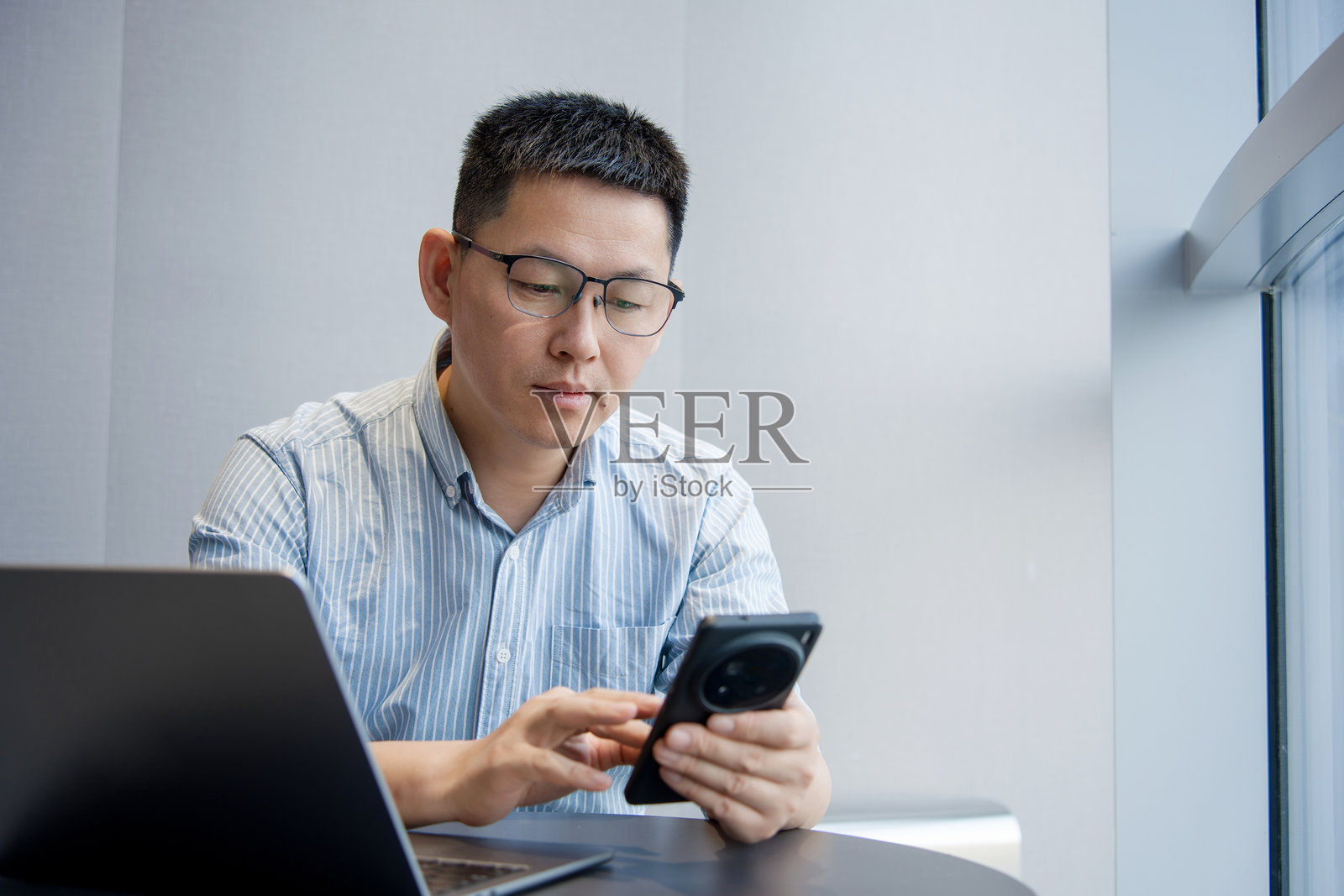 戴眼镜男子办公桌前用手机查资料照片摄影图片