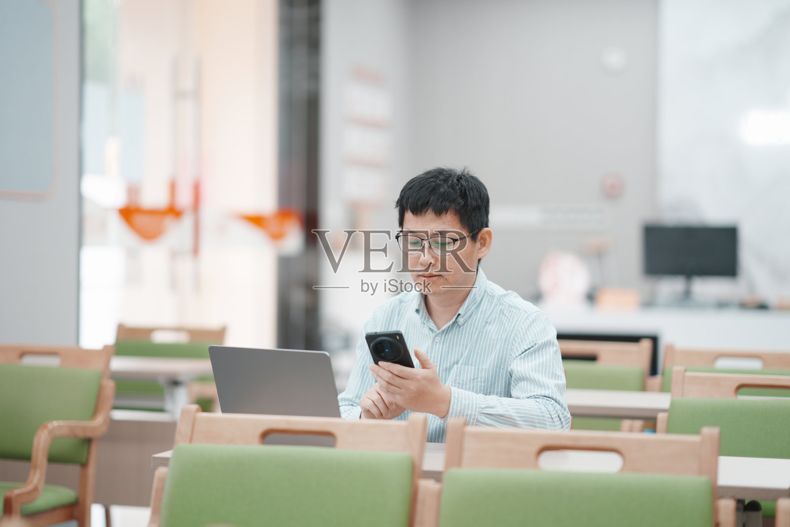 戴眼镜男子图书馆用手机看信息照片摄影图片