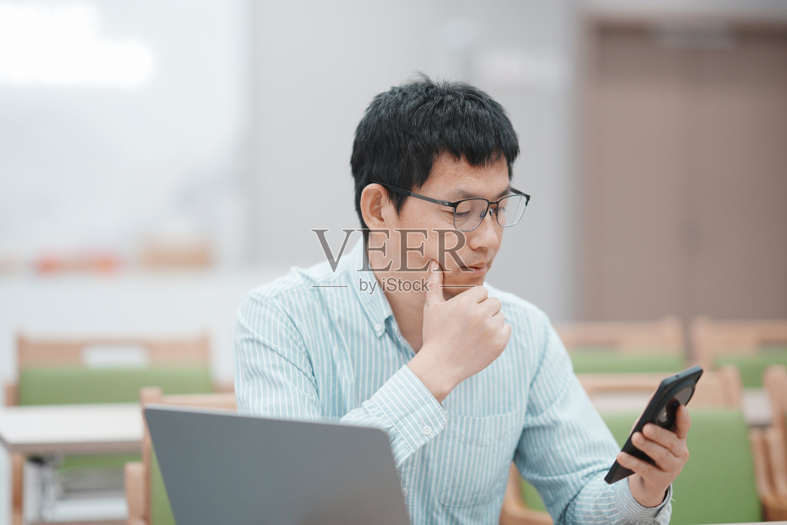 戴眼镜男子思考时看手机用笔记本电脑照片摄影图片