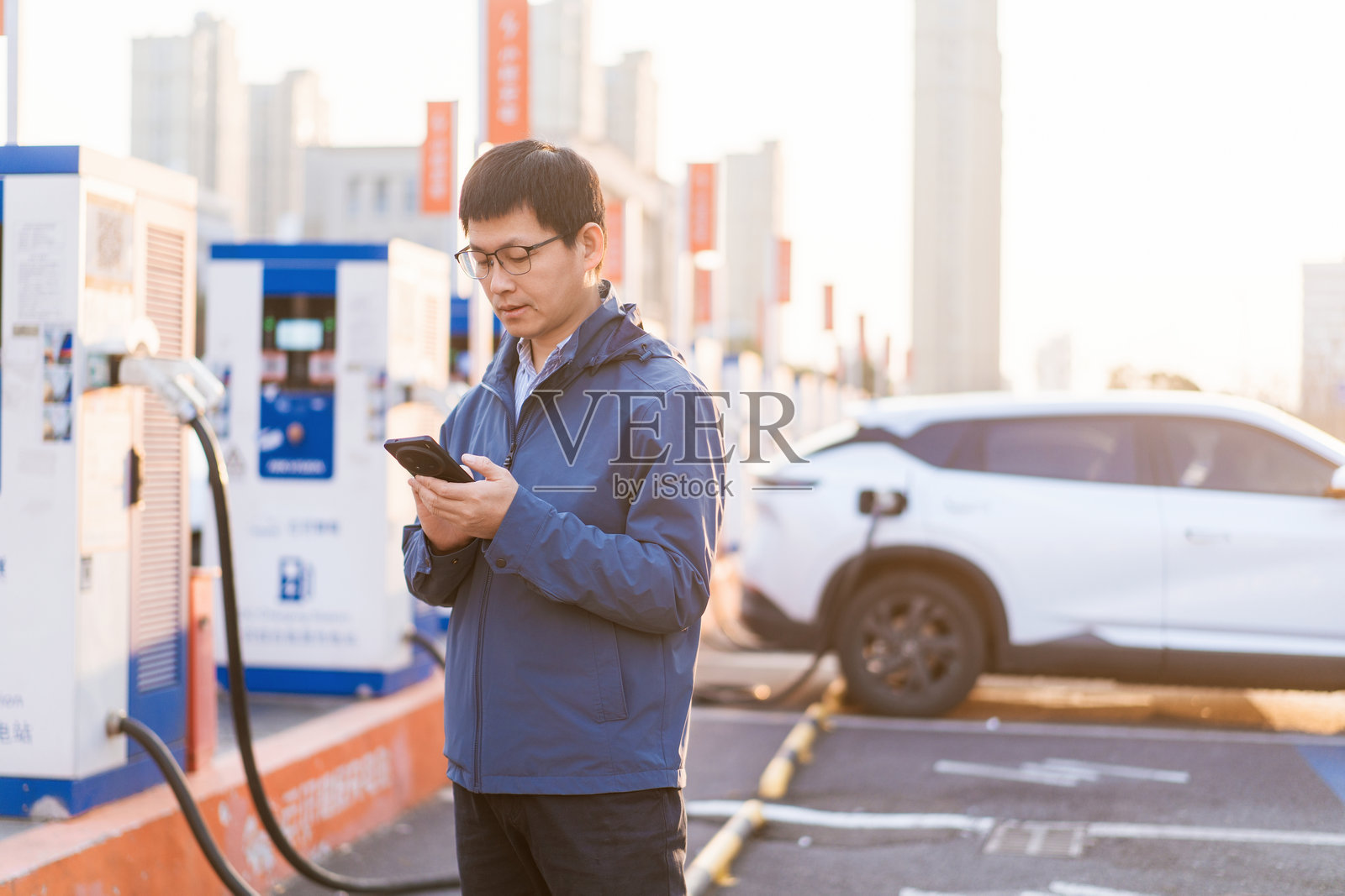 男子充电站旁看手机白色电车在充照片摄影图片