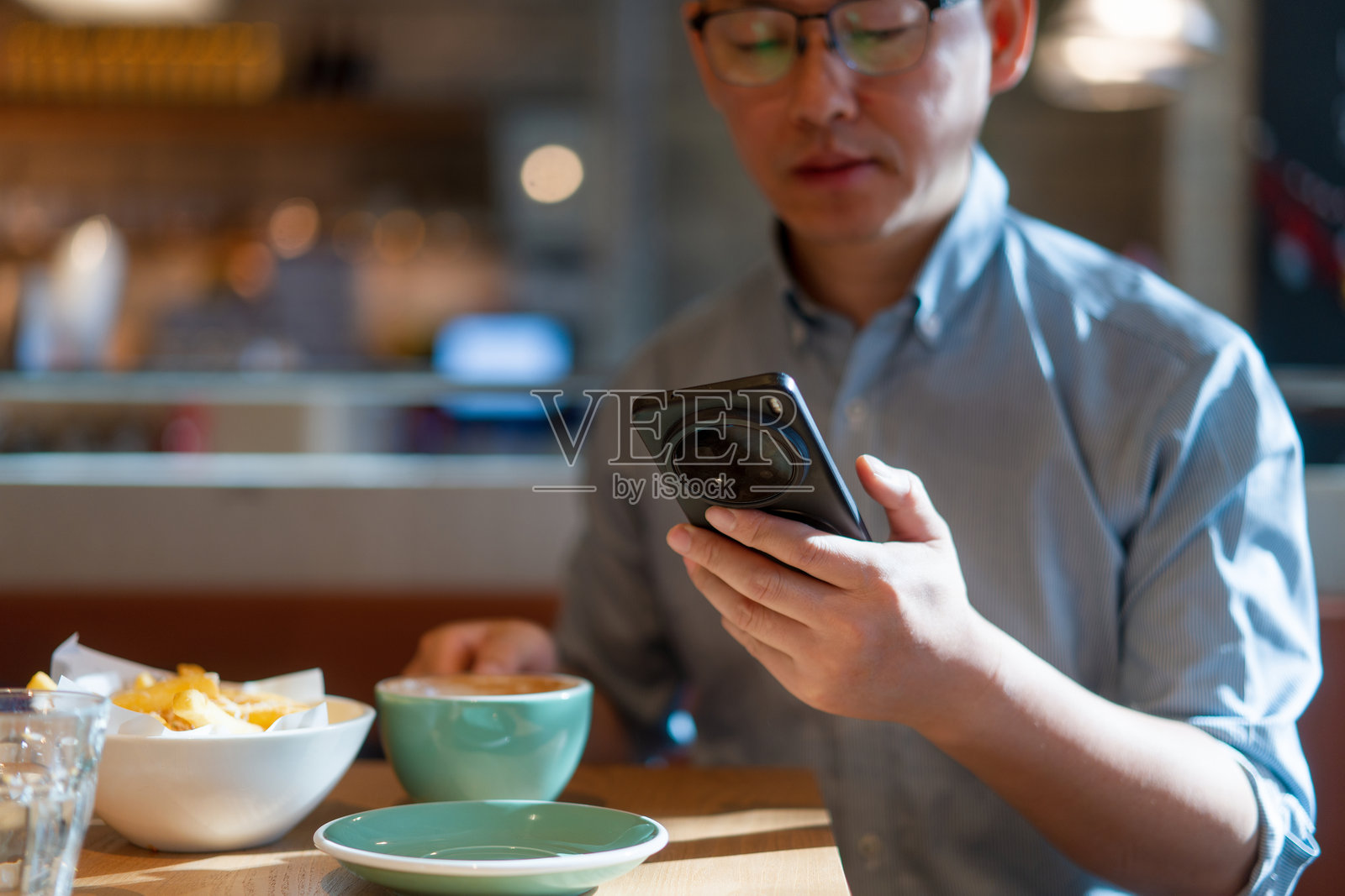 戴眼镜男子咖啡馆用手机看屏幕照片摄影图片