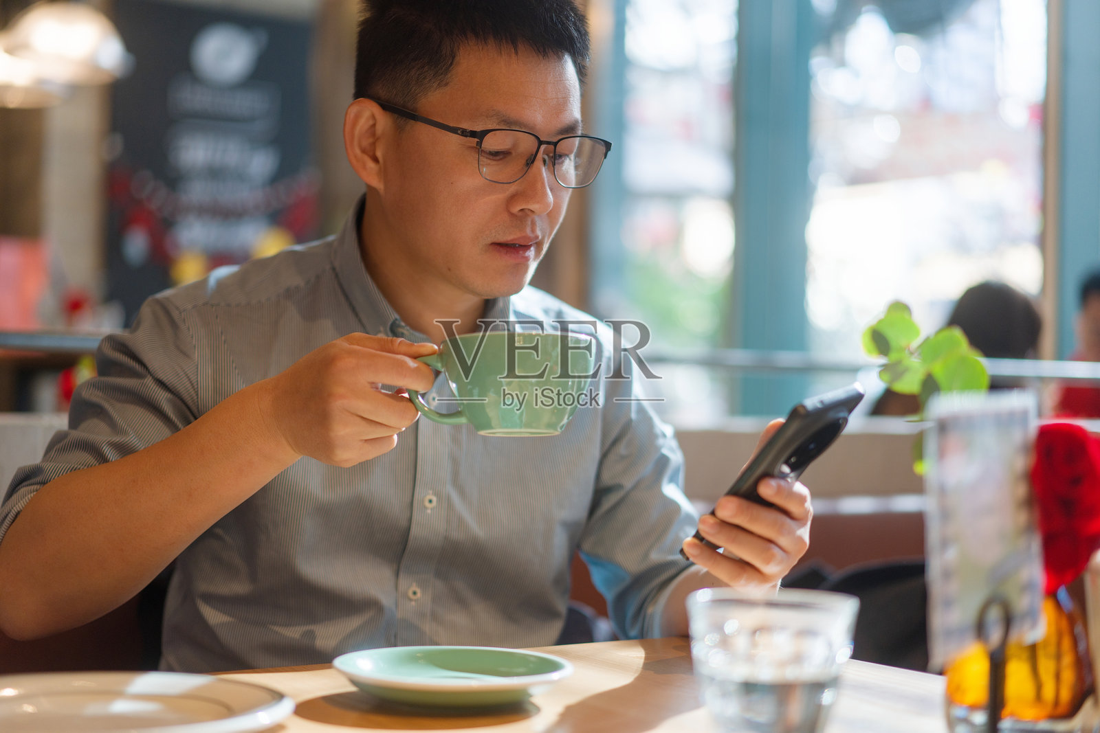 戴眼镜男子咖啡馆手持茶杯看手机照片摄影图片