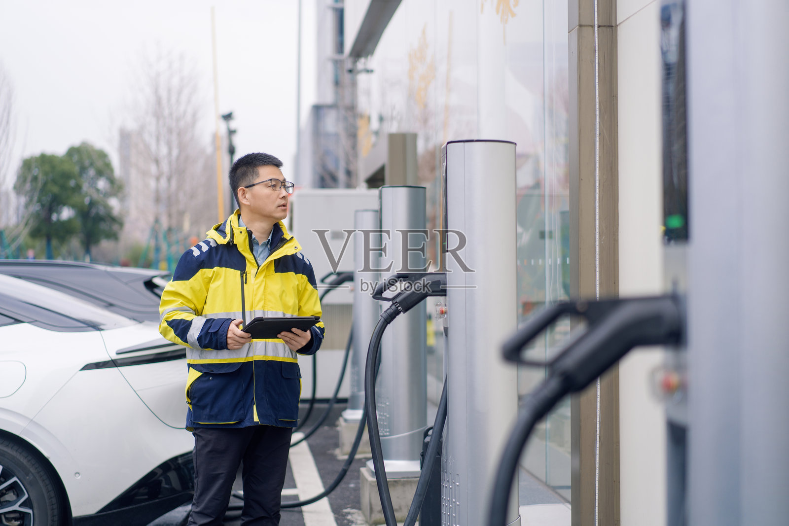身穿黄蓝工装男子手持平板检查充电桩照片摄影图片