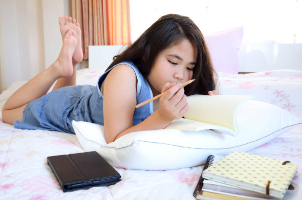 小女孩在床上写书。图片下载