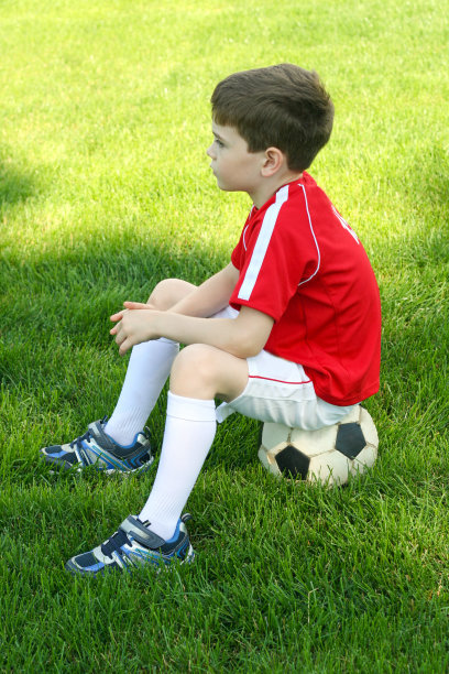 一个男孩坐在足球上图片下载