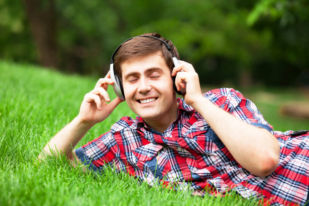 英俊的年轻人戴着耳机在绿草地上图片下载