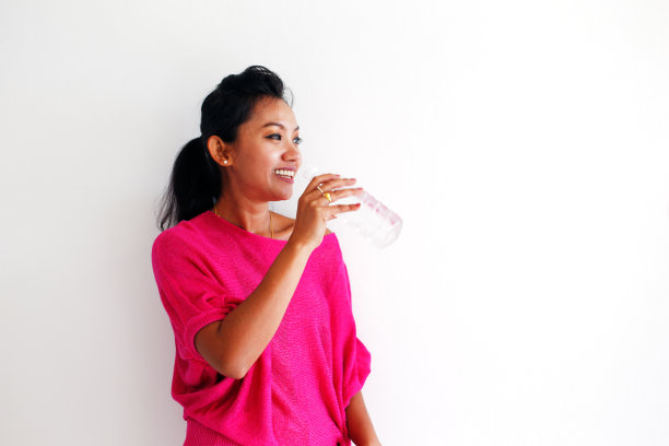 一个年轻女子，靠着一堵白墙喝水图片下载