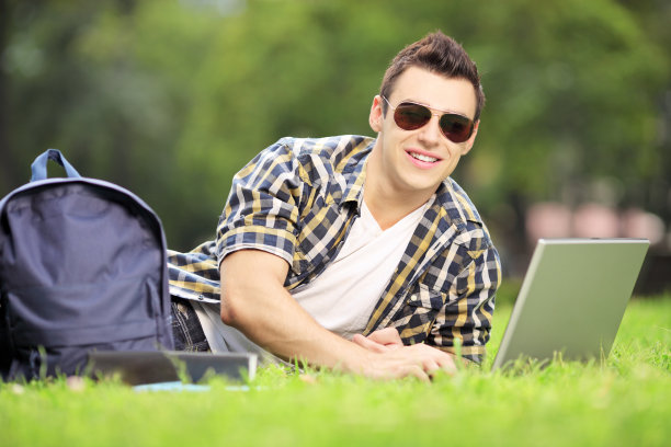 微笑的男学生在公园里用笔记本电脑工作图片下载