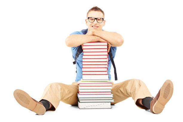 男同学微笑着拿着书包放在一堆书上图片下载