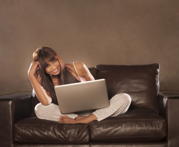 年轻迷人的女人微笑在沙发上与电脑图片下载