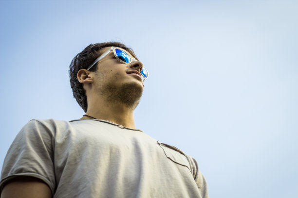 年轻男子戴着带有蓝天背景的太阳镜图片下载