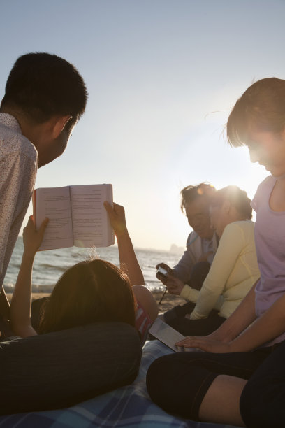 几代同堂的家庭在海滩上放松和阅读图片下载