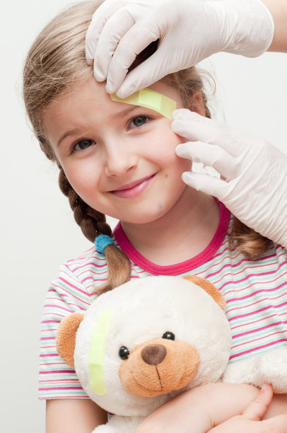 女孩抱着带乳胶手套的泰迪熊，把橡皮膏敷在头上图片下载