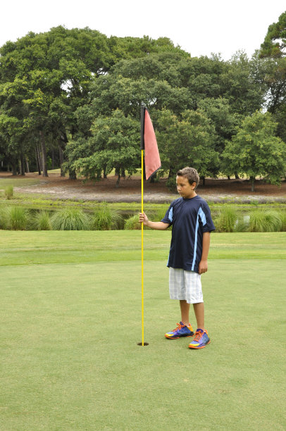 小男孩在高尔夫球场上举着旗子图片下载
