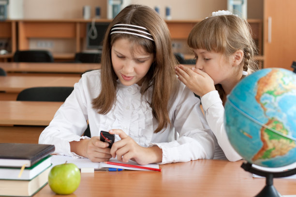 两个女孩坐在课桌前，手里拿着手机图片下载