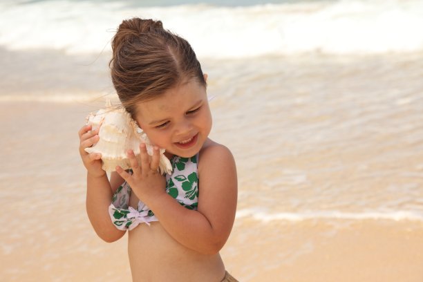 年轻的女孩站在海滩上，把贝壳举到耳朵边图片下载