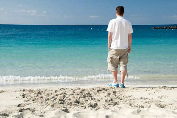 一个穿着短裤的男人在度假，在海滩上散步图片下载