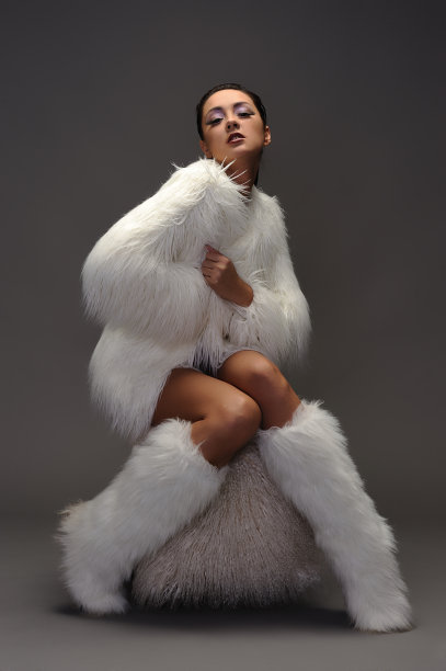 穿着白色裘皮大衣的年轻女子坐在软垫椅上图片下载