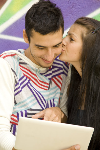 一对情侣在涂鸦墙旁边带着笔记本。图片下载