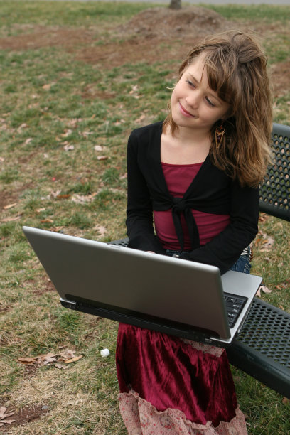 小女孩坐在公园的长椅上玩电脑图片下载