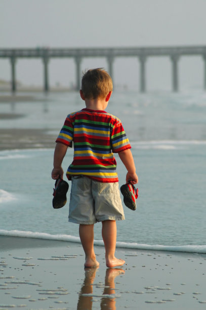 小男孩拿着鞋子在海边图片下载