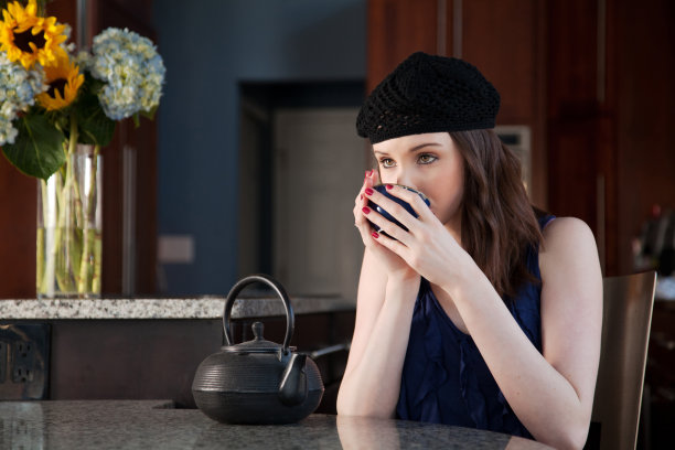 美丽的女人在厨房里喝茶，手里拿着花图片下载