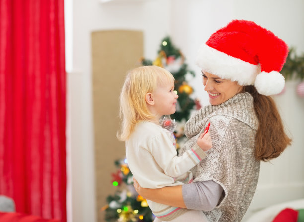 快乐的年轻母亲抱着婴儿靠近圣诞树图片下载