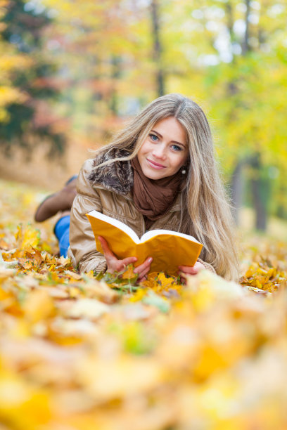 年轻女子躺在树叶上看书图片下载