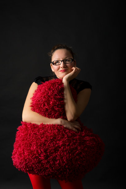 微笑的年轻女子拿着一颗大的毛茸茸的红心。图片下载