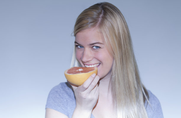 年轻快乐的女人吃葡萄柚的肖像图片下载