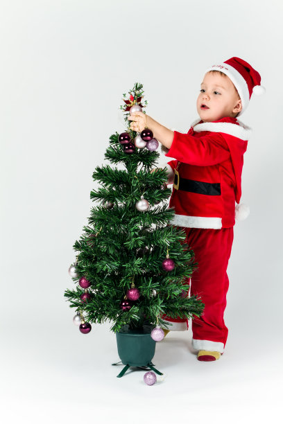 小男孩装扮成圣诞老人装饰圣诞树，挂起来图片下载