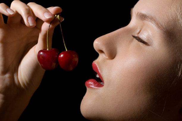 性感女人的肖像与樱桃在黑色的背景图片下载