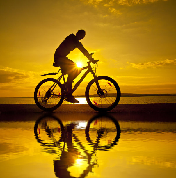 一个骑自行车的人的剪影在日落与水的倒影图片下载
