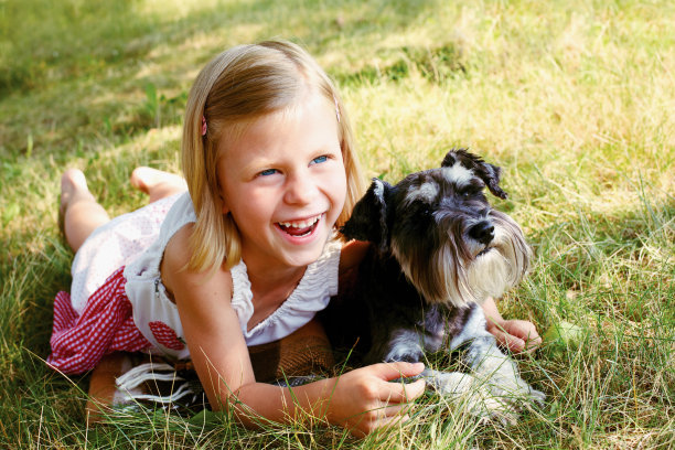 可爱的女孩抱着她的狗坐在草地上图片下载