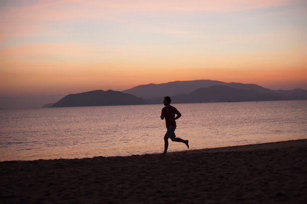 日落时沙滩上跑步者的剪影图片下载