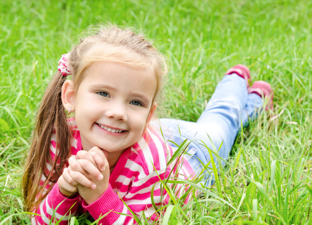 可爱的微笑小女孩躺在草地上的肖像图片下载