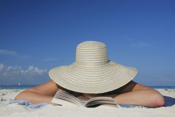 一个女人戴着太阳帽躺在沙滩上看书的照片图片下载