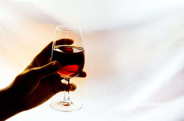 手里拿着背光的红酒酒杯图片下载