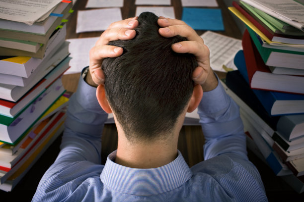 年轻人沮丧地坐在成堆的书旁边图片下载