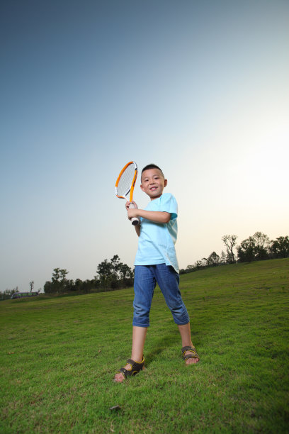 一个亚洲男孩在草坪上打网球图片下载