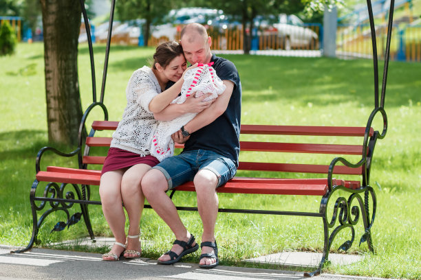 年轻的一家人坐在公园的长椅上。图片下载
