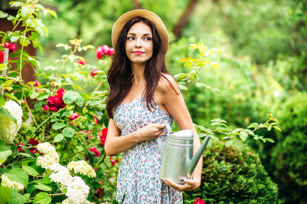 年轻微笑的女人戴着帽子和喷壶在花园里图片下载