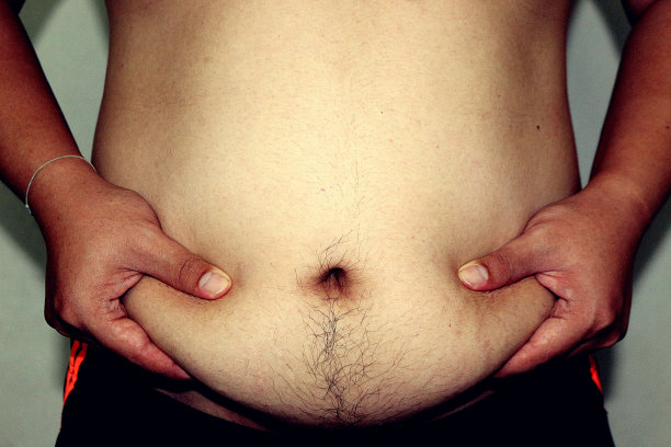 一个男人抓着他腹部多余脂肪的特写图片下载