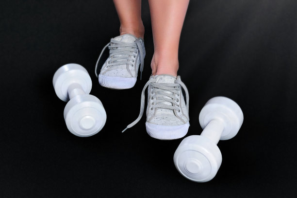 脚穿白色运动鞋，白色哑铃，背景是黑色图片下载
