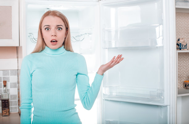年轻的金发女郎在家冰箱旁边图片下载